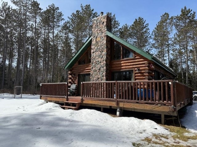 snow covered property featuring log siding, a wooden deck, and a chimney