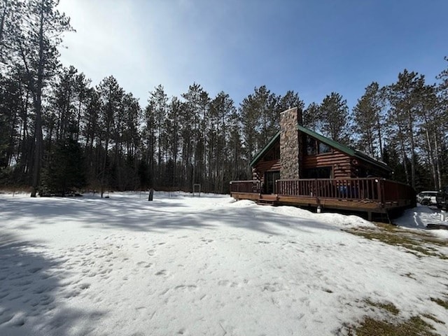 snow covered rear of property featuring a chimney, a wooden deck, and log siding