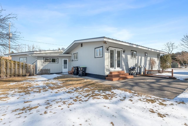 snow covered rear of property featuring french doors and fence