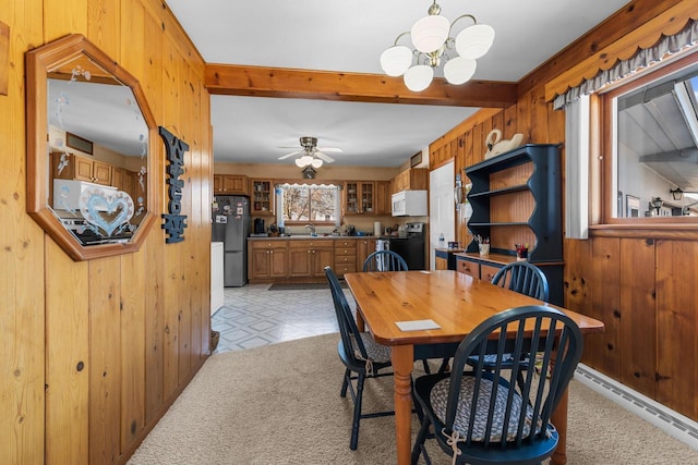 dining space with wooden walls, a baseboard heating unit, light floors, light carpet, and ceiling fan with notable chandelier