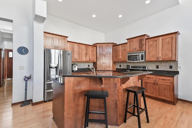 kitchen with tasteful backsplash, a breakfast bar, appliances with stainless steel finishes, brown cabinetry, and a kitchen island with sink