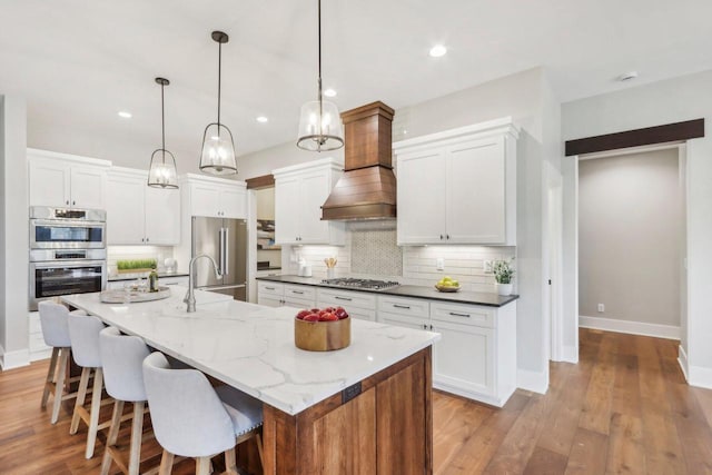 kitchen with custom range hood, backsplash, stainless steel appliances, light wood-style floors, and a breakfast bar area