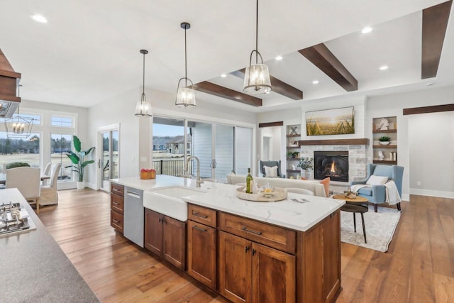 kitchen with stainless steel appliances, a stone fireplace, hardwood / wood-style flooring, a sink, and beamed ceiling