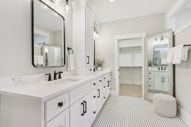 bathroom with double vanity, a spacious closet, baseboards, and a sink