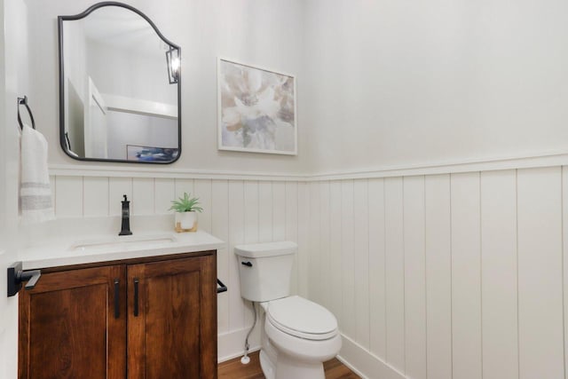 bathroom featuring vanity, toilet, and a wainscoted wall