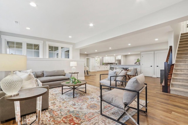 living area featuring visible vents, baseboards, stairway, light wood-type flooring, and recessed lighting