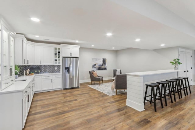 kitchen featuring light countertops, tasteful backsplash, wood finished floors, and stainless steel refrigerator with ice dispenser