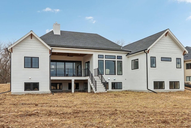 back of house featuring roof with shingles, a yard, a sunroom, a chimney, and stairs