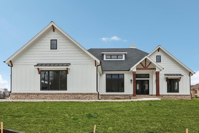 back of property with a yard, roof with shingles, board and batten siding, and brick siding