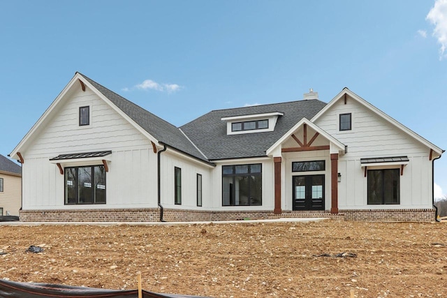 back of house with a chimney, a shingled roof, french doors, board and batten siding, and brick siding