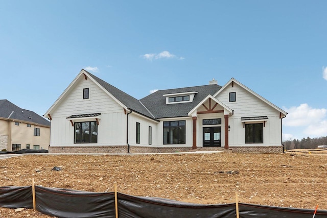 modern inspired farmhouse featuring brick siding, board and batten siding, a chimney, and roof with shingles