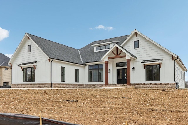 modern farmhouse featuring brick siding, board and batten siding, and roof with shingles