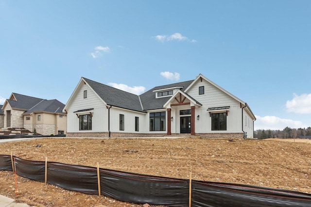 modern inspired farmhouse with brick siding, roof with shingles, and fence