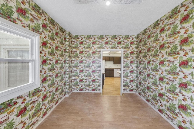 unfurnished room featuring wallpapered walls, baseboards, light wood-type flooring, and a textured ceiling