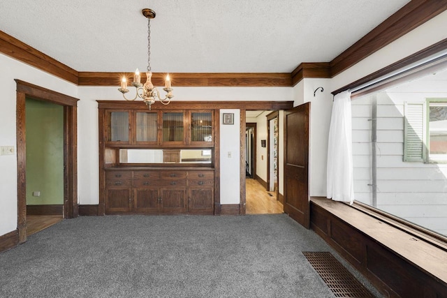 unfurnished dining area with baseboards, carpet floors, a textured ceiling, crown molding, and a chandelier