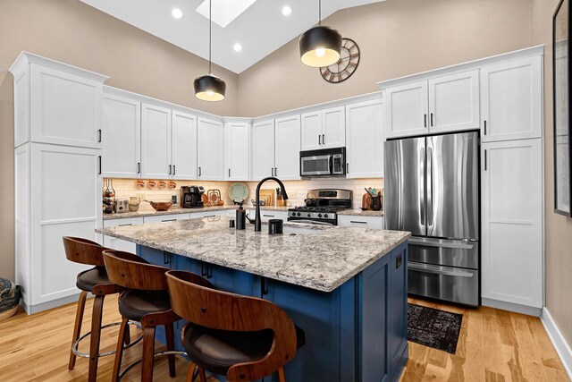 kitchen featuring a skylight, white cabinets, appliances with stainless steel finishes, a kitchen bar, and light wood-type flooring