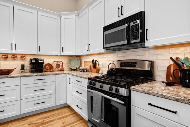 kitchen with tasteful backsplash, light stone countertops, stainless steel range with gas stovetop, light wood-style flooring, and white cabinetry