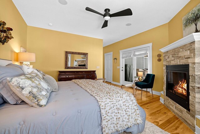 bedroom with light wood finished floors, a stone fireplace, ceiling fan, and baseboards