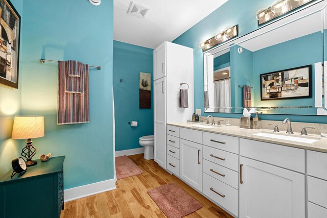 bathroom featuring a sink, toilet, wood finished floors, and double vanity