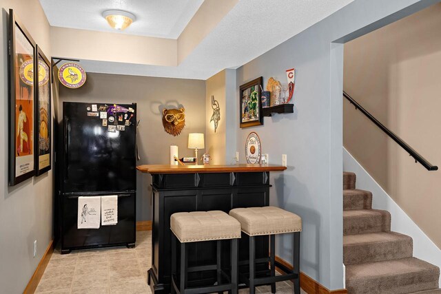 bar featuring stairway, baseboards, a bar, and freestanding refrigerator