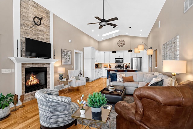 living room featuring a ceiling fan, visible vents, high vaulted ceiling, light wood-style flooring, and a fireplace