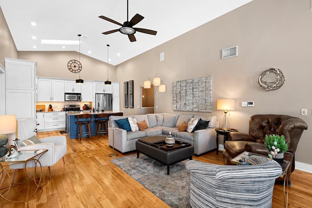 living area featuring light wood finished floors, visible vents, high vaulted ceiling, and a ceiling fan