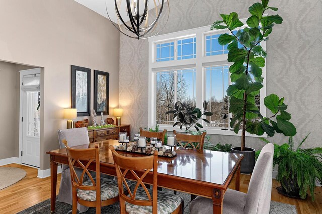 dining space with a chandelier, a towering ceiling, baseboards, and wood finished floors