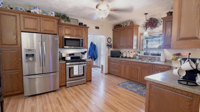 kitchen with a sink, stainless steel appliances, brown cabinetry, and light wood finished floors