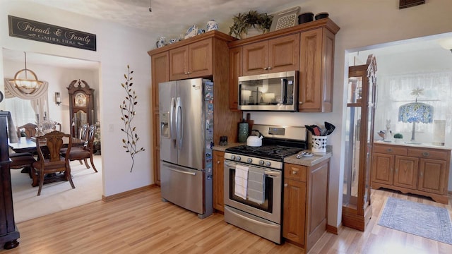 kitchen featuring light wood-type flooring, brown cabinets, appliances with stainless steel finishes, an inviting chandelier, and baseboards