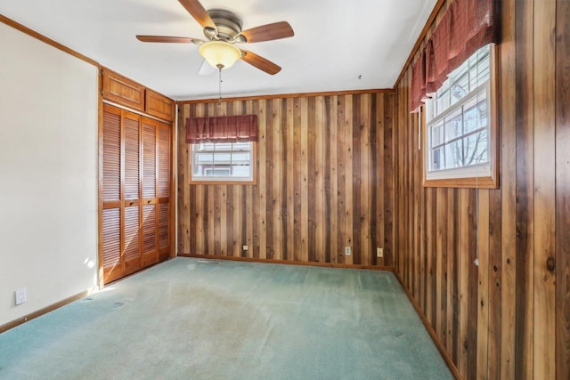 carpeted spare room featuring a ceiling fan, baseboards, wood walls, and ornamental molding