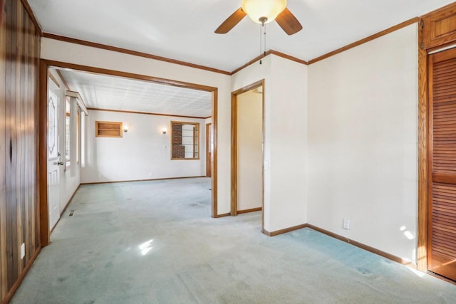 spare room featuring crown molding, a ceiling fan, baseboards, and light carpet