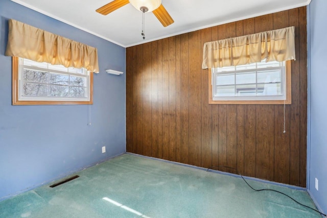 spare room with wooden walls, visible vents, ceiling fan, and carpet