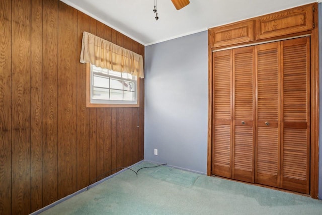 unfurnished bedroom featuring a closet, carpet floors, wooden walls, and crown molding