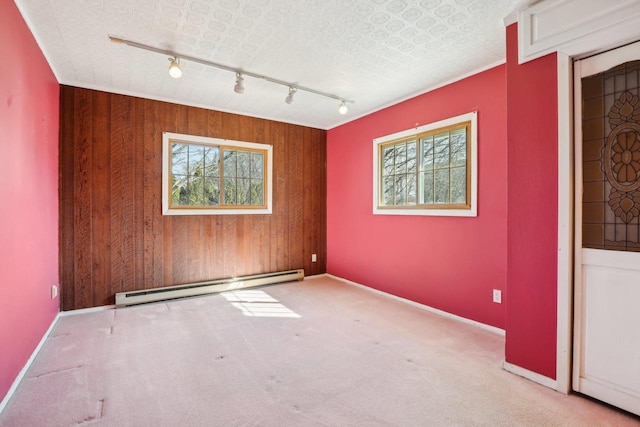 empty room featuring baseboards, baseboard heating, track lighting, and carpet flooring