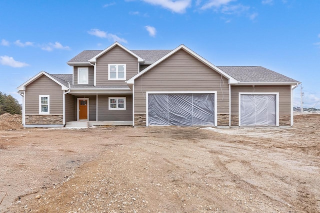 view of front of property with dirt driveway, a garage, stone siding, and roof with shingles