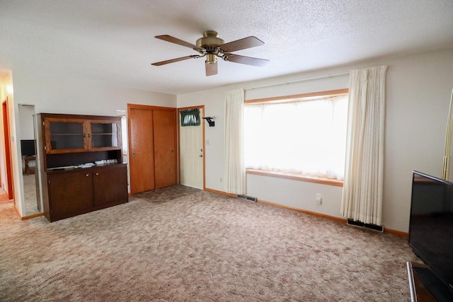 unfurnished living room with visible vents, ceiling fan, baseboards, carpet floors, and a textured ceiling