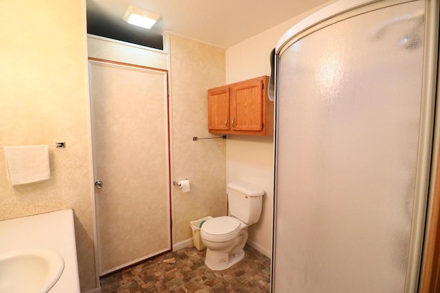 bathroom with a stall shower, toilet, and baseboards