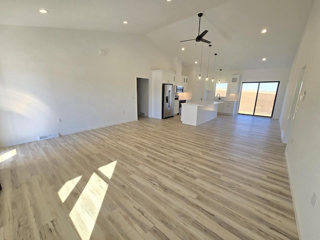 unfurnished living room with baseboards, visible vents, high vaulted ceiling, ceiling fan, and light wood-type flooring