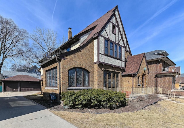 view of side of property featuring brick siding, a chimney, a garage, a balcony, and an outbuilding