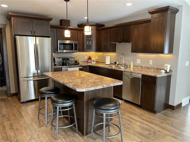 kitchen featuring dark brown cabinetry, a kitchen bar, appliances with stainless steel finishes, light wood-style floors, and a sink