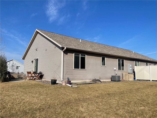 rear view of house featuring central air condition unit, a lawn, and roof with shingles