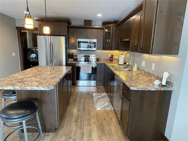 kitchen with a sink, light wood-style floors, appliances with stainless steel finishes, dark brown cabinets, and washer / dryer