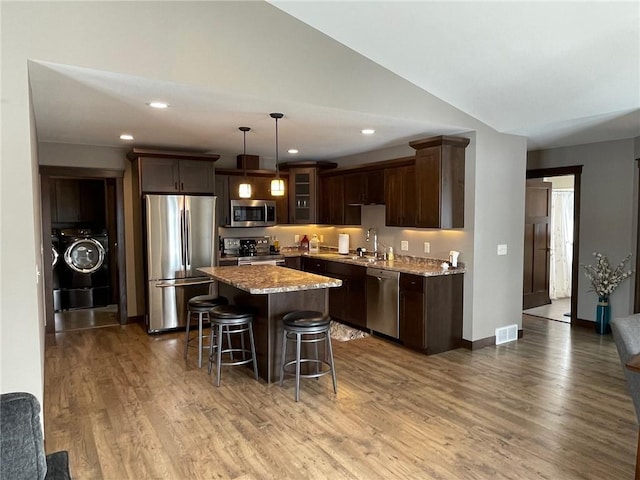 kitchen with a sink, stainless steel appliances, wood finished floors, and a center island