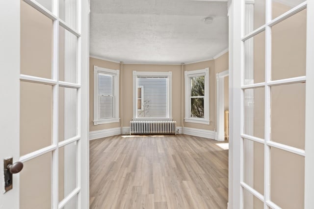 interior space featuring french doors, baseboards, light wood-style flooring, and radiator heating unit