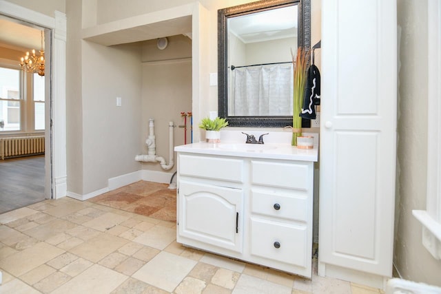 full bath featuring vanity, stone tile floors, radiator, baseboards, and a notable chandelier