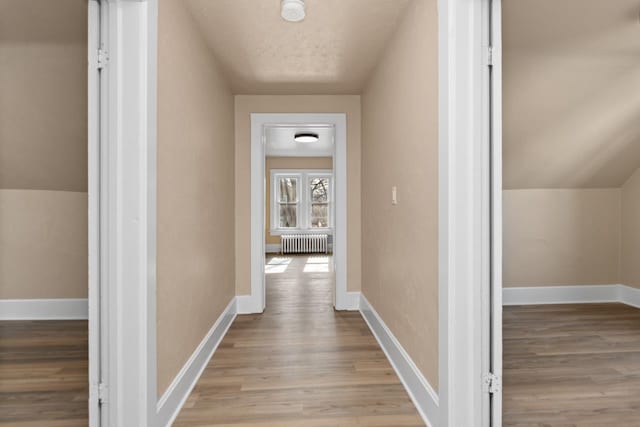 hallway featuring baseboards, wood finished floors, and radiator heating unit