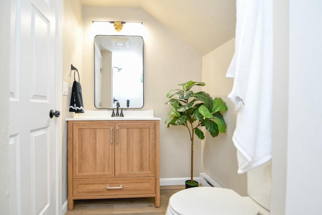 bathroom with vanity, wood finished floors, a baseboard radiator, lofted ceiling, and toilet