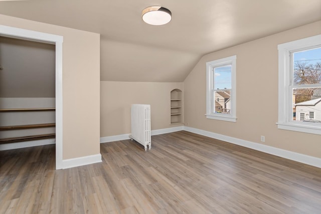 bonus room featuring radiator, baseboards, built in features, vaulted ceiling, and wood finished floors