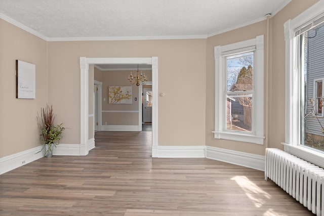 empty room with ornamental molding, radiator heating unit, baseboards, and wood finished floors