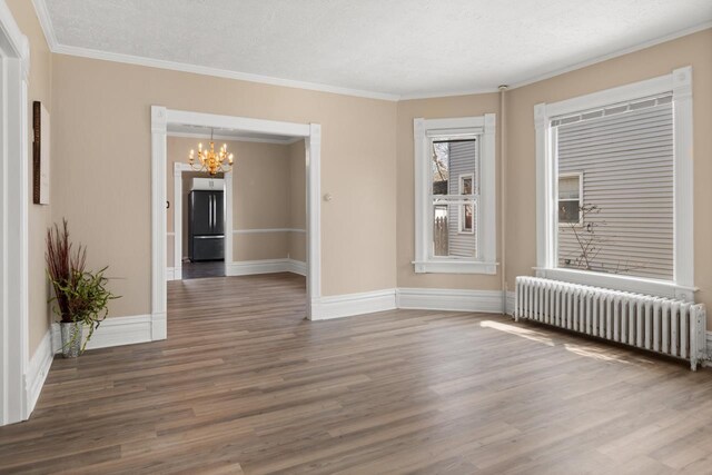 empty room featuring wood finished floors, radiator, a chandelier, and crown molding